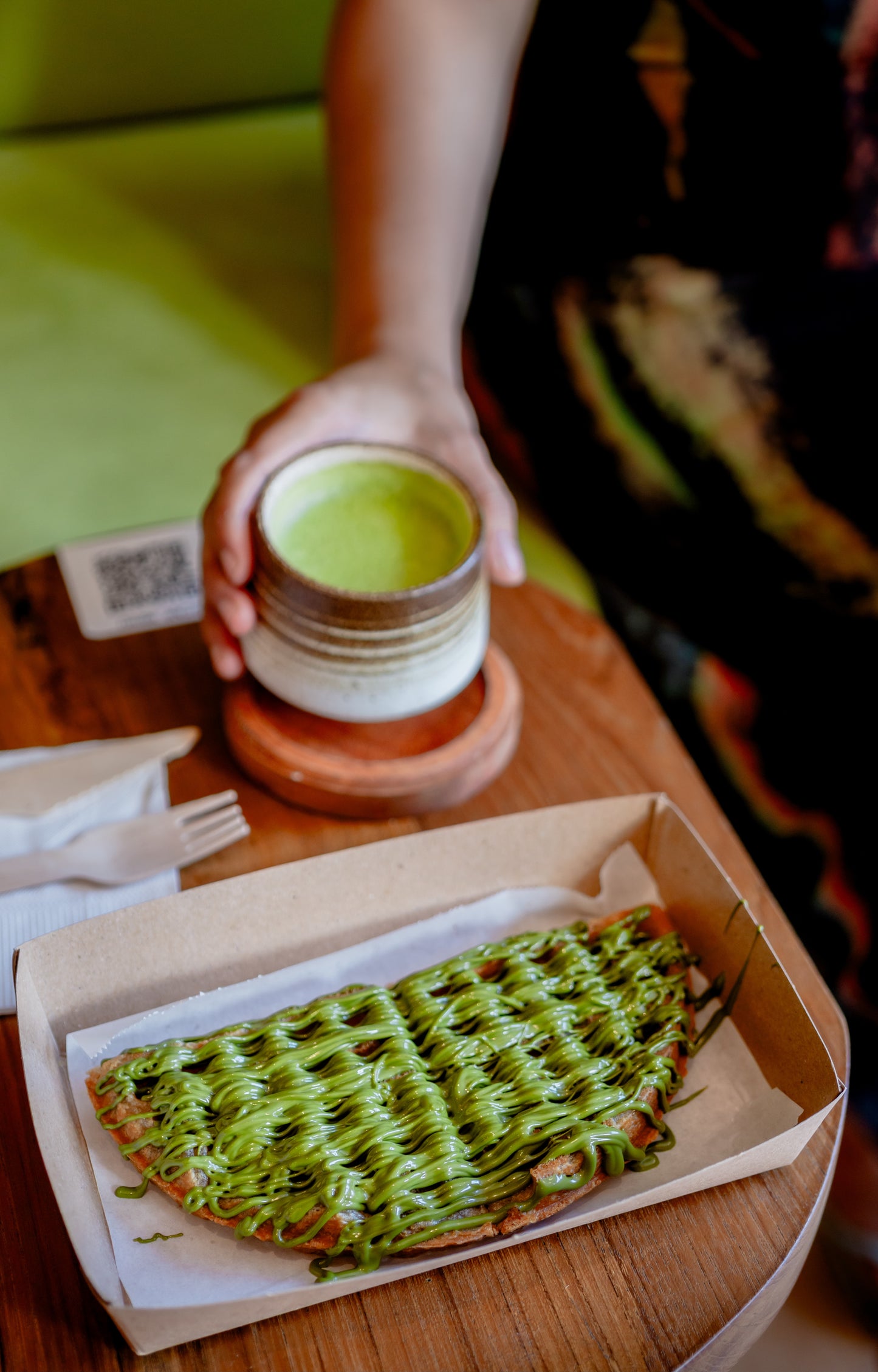 Matcha spread on a waffle. Person holding a matcha drink in the background.