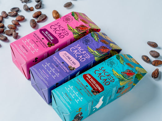 Three different coloured boxes of cacao chocolate with cacao beans scattered around.