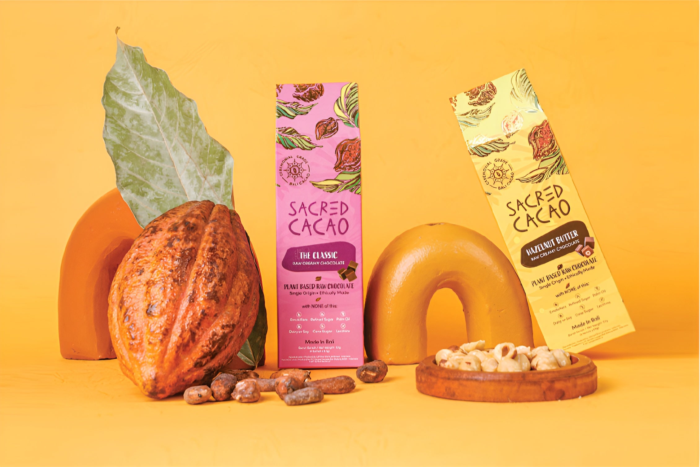 Two Sacred Cacao chocolate cartons surround by natural cacao items.